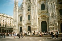 many people are walking around in front of an old building that is very tall and ornate