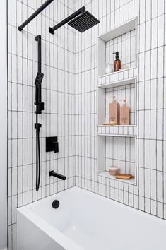 a white bath tub sitting next to a black and white tiled shower head mounted on a wall