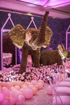 an elephant statue surrounded by balloons and streamers in a room filled with pink flowers