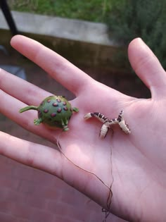 a hand holding two small toy animals on it's palm, one is green and the other is brown