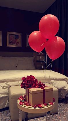 three red balloons are floating over a gift box on a table in front of a bed