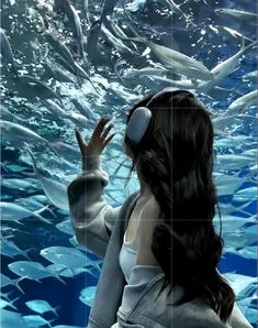 a woman standing in front of an aquarium with fish swimming around her and wearing headphones