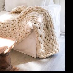 a large chunky blanket sitting on top of a wooden table next to a white couch