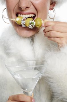 a woman in a white fur coat holding a olive and toothbrush to her mouth