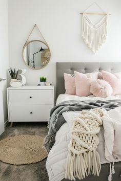 a bedroom with white walls and grey bedding, pink pillows on the headboard