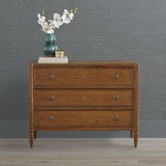 a wooden dresser with flowers on top and a green vase sitting on top of it