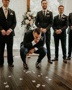 a man kneeling down in front of a group of men wearing suits and tie standing next to each other