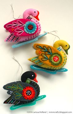 three colorful birds hanging from strings on a white surface