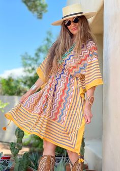 Our Nizhoni midi dress, which means ‘beautiful’ in Navajo, is designed to bring beauty and charm to your day. The wide colorful border complements the traditional native zigzag pattern that is popular in American Indian design. With vertical lines and bold joyful colors, this kaftan lengthens and slims. Tassels are hand made and hand beaded. 100% cotton, delicate cold machine wash in a lingerie bag to protect tassels or hand wash cold, hang dry. Length is 39" One size with adjustable drawstring Multicolor Ikat Print Kaftan Tunic, Bohemian Striped Dresses For Vacation, Bohemian Striped Vacation Dresses, Bohemian Multicolor Print Midi Dress, Bohemian Multicolor Pattern Midi Dress, Multicolor Geometric Pattern Dress For Vacation, Multicolor Bohemian Dress With Geometric Pattern, Bohemian Multicolor Geometric Pattern Dress, Multicolor Geometric Pattern Vacation Dress