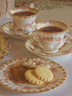 two tea cups and saucers filled with cookies on a white tablecloth covered table