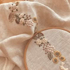 two embroidery hoops with flowers on them sitting next to a piece of cloth that has been stitched together