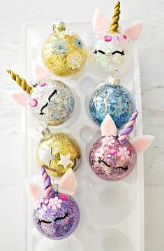 an assortment of christmas ornaments with unicorn faces and stars on them in a plastic container