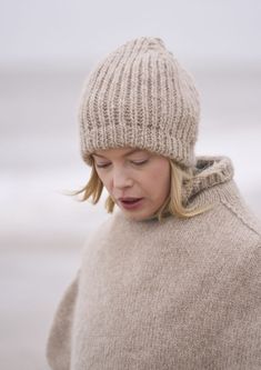 a woman with her eyes closed wearing a knitted hat and looking down at her cell phone