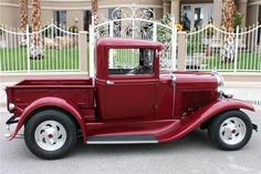 an old red truck is parked in front of a white fence and gated area