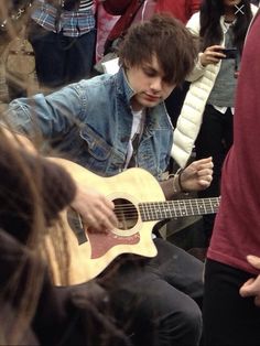 a young man playing an acoustic guitar in front of a group of people with cell phones