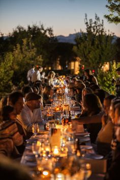 a group of people sitting at a long table with candles on it in front of them