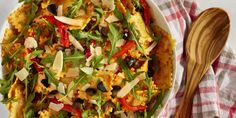 a white plate topped with pasta covered in cheese and veggies next to a wooden spoon