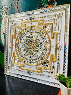 an intricately designed white and gold wall hanging in front of a potted plant