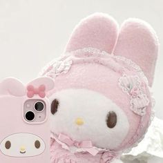 a pink hello kitty cell phone case sitting next to a white stuffed animal toy with a bow on it's head