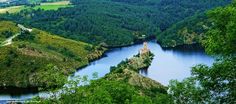 an aerial view of a lake surrounded by trees and hills in the distance with a castle on top