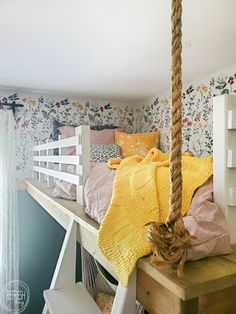 a bed with a rope hanging from it's side in a room that has floral wallpaper on the walls