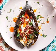 a white plate topped with an eggplant covered in sauce and garnish