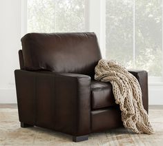 a brown leather chair with a blanket on top of it in front of a window