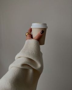 a woman's hand holding a cup of coffee in her left hand and wearing a white sweater