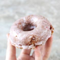 a person holding a donut with icing and nuts in their hand on concrete