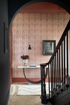 a hallway with pink wallpaper and black bannister next to the stair case