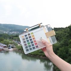 a person holding up a water color swatch in front of a body of water