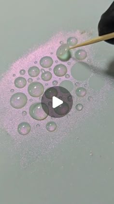 a person is using an object to paint bubbles on the surface with pink and purple colors