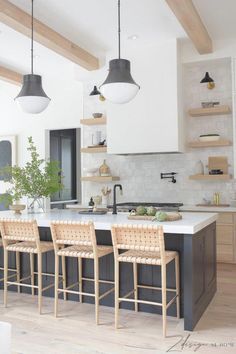 a kitchen island with four stools in front of it and two hanging lights above it