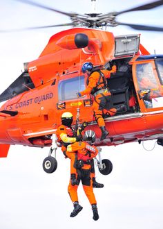 two men in orange suits are standing next to an orange helicopter