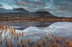 the mountains are reflected in the still water at sunrise or sunset, as clouds loom over them