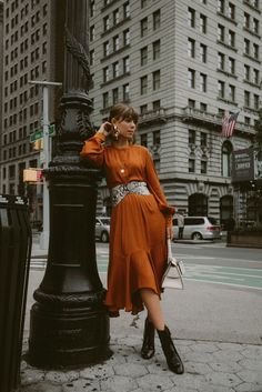 a woman in an orange dress leaning against a lamp post