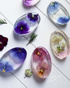 six different colored glass flowers in oval dishes on a white table with wood planks