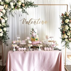 a table topped with lots of desserts next to a white and pink flower covered wall