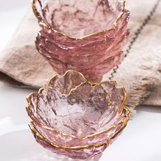 three pink glass bowls sitting on top of a white table next to a silver chain