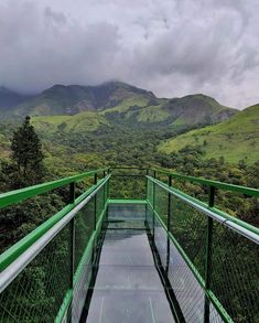 a green bridge with mountains in the background and clouds above it on a cloudy day