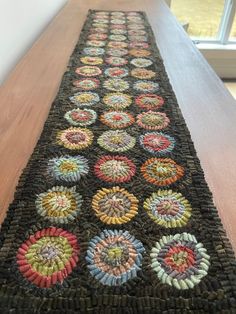 a long table runner with multicolored circles on the edge and bottom, sitting on a wooden surface