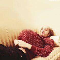 a man laying on top of a white couch next to a woman in a red shirt