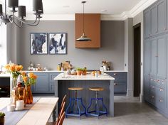 a kitchen with blue cabinets and stools in the center is decorated with orange flowers