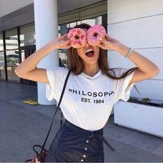 a woman holding two donuts up to her face with both hands while standing in front of a building