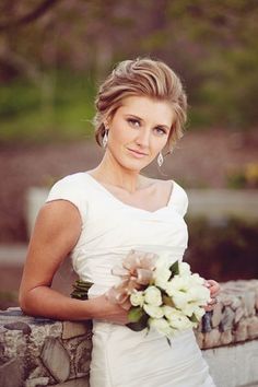 a woman in a white dress is holding a bouquet and standing on a stone wall