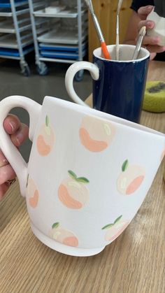 a hand holding a coffee cup with peaches painted on the outside and inside it