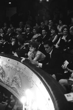 a black and white photo of people sitting in an auditorium with their hands on the seats