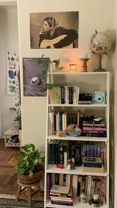 a bookshelf filled with lots of books next to a lamp and pictures on the wall