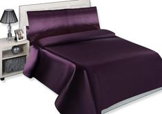 a bed with a purple comforter and night stand