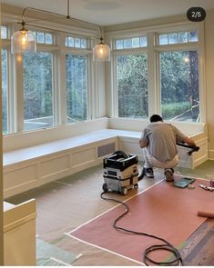 a man working on the floor in an empty room with large windows and hard wood floors